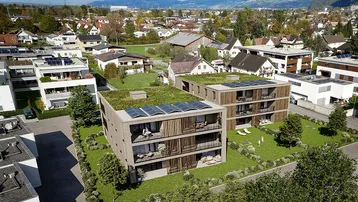 Luftaufnahme von modernen Wohngebäuden mit begrünten Dächern und Photovoltaikanlagen in ländlicher Umgebung.