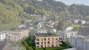Luftaufnahme eines modernen Wohngebäudes mit Holzfassade und Photovoltaikanlage in grüner Umgebung.