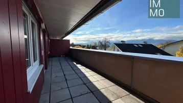 Lange Loggia mit Fliesenboden und weitem Blick auf die umliegende Wohngegend unter blauem Himmel.