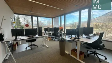 Geräumiges Großraumbüro mit mehreren modernen Arbeitsplätzen, großen Fenstern und Bergblick.