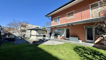 Gepflegter Gartenbereich mit Rasenfläche, Steinterrasse und Außengrill hinter dem Haus.