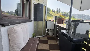 Sonniger Balkon mit Sitzbank, Sonnenschirm und weitem Blick auf die grüne Landschaft.