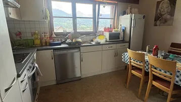 Gemütliche Küche mit Essbereich, weißen Schränken, Holzdecke und Bergblick durch das Fenster.
