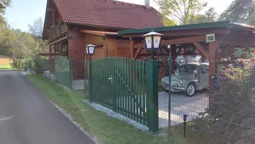 Ansicht des Holzhauses mit Carport und einem Oldtimer auf dem gepflasterten Vorplatz.