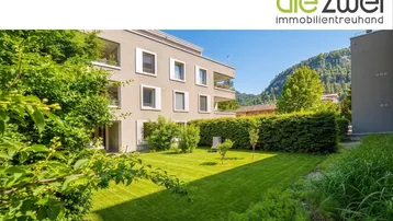 Gepflegter Gartenbereich mit Rasenfläche und Hecke vor der modernen Wohnanlage.