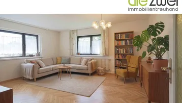 Helles Wohnzimmer mit Parkettboden, beigem Sofa und Bücherregal, ideal zum Entspannen.