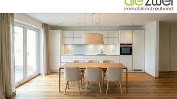 Moderne Küche mit weißen Schränken, Holzboden und Essbereich, mit Zugang zu einem Balkon.