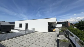 Geräumige Dachterrasse mit grauen Fliesen, Metallgeländer und weitem Blick über die Umgebung und Berge.