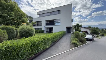 Modernes Mehrfamilienhaus mit gepflegter Grünanlage und Zufahrt von der Straße.