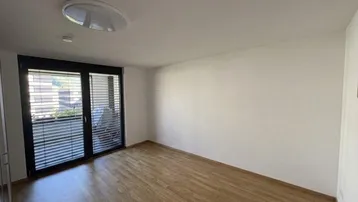 Helles Schlafzimmer mit Holzparkettboden und großem Fenster, das viel Tageslicht hereinlässt.