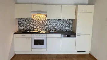Helle Einbauküche mit weißen Schränken, dunkler Arbeitsplatte und Mosaikfliesen als Spritzschutz.
