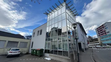 Moderne Architektur mit großer Glasfassade und angrenzendem Parkplatz unter bewölktem Himmel.
