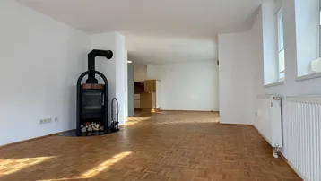 Geräumiger Wohnbereich mit Parkettboden, einem modernen Holzofen und großen Fenstern.
