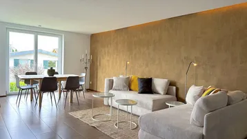 Heller Wohn- und Essbereich mit modernem Sofa, Esstisch und großen Fenstern.
