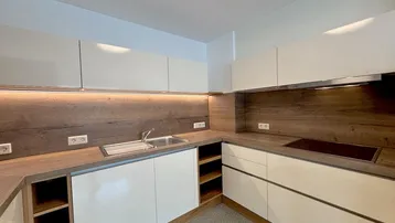 Moderne Einbauküche mit weißen Fronten, Holz-Arbeitsplatten und integriertem Kochfeld.