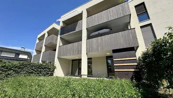 Moderne Wohnanlage mit mehreren Balkonen und begrüntem Vorgarten unter blauem Himmel.