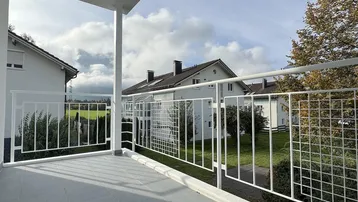 Heller Balkon mit modernem Geländer und Blick ins Grüne.
