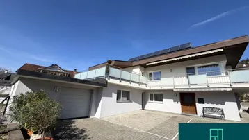 Modernes Wohnhaus mit Garage, gepflasterter Auffahrt und mehreren Balkonen unter blauem Himmel.