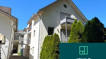 Mehrfamilienhaus mit mehreren Balkonen und gepflegten Büschen unter blauem Himmel.