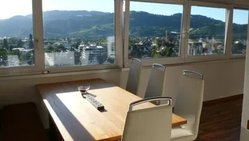 Heller Essbereich mit Holztisch, modernen Stühlen und weitem Blick über die Stadt und Berge.