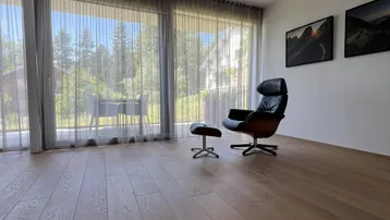 Heller Wohnbereich mit bequemem Sessel und großen Fenstern mit Blick ins Grüne.