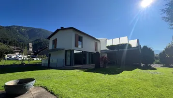 Modernes Haus mit großem, gepflegtem Rasen und Bergblick unter strahlend blauem Himmel.