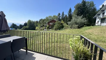 Großer Balkon mit Esstisch und Stühlen, bietet einen weiten Blick über grüne Felder.