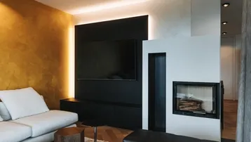 Modernes Wohnzimmer mit Kamin, großem Fernseher und einer auffälligen goldenen Akzentwand.