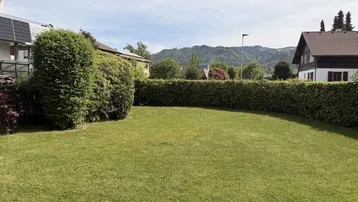 Großer, gepflegter Rasenbereich mit Hecke und Blick auf die umliegende Hügellandschaft.