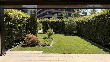 Gepflegter Garten mit Rasenfläche und hohen Hecken, von einer überdachten Terrasse aus gesehen.