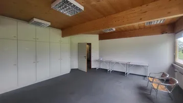 Geräumiges Büro mit hohen Decken, Holzbalken und Einbauschränken, gut beleuchtet durch große Fenster.