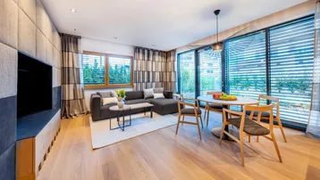 Moderner offener Wohn-Essbereich mit Holzboden, bequemer Sitzecke und Esstisch. Große Fenster lassen viel Licht herein.