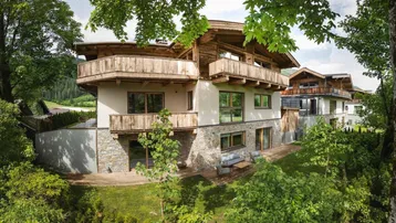 Modernes Chalet mit Holzfassade, Steinakzenten und mehreren Balkonen in grüner Umgebung.