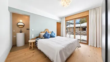 Gemütliches Schlafzimmer mit Holzboden, großem Fenster und integriertem Waschbeckenbereich.