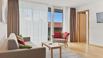 Gemütlicher Wohnbereich mit Sofa, Sessel und großen Fenstern zum Außenbereich.