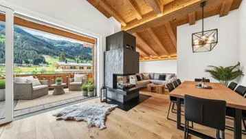 Geräumiger Wohn-Essbereich mit modernem Kamin, Holzbalkendecke und Zugang zu einem Balkon mit Bergblick.