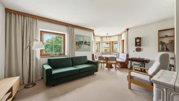 Gemütlicher Wohn-Essbereich mit grünem Sofa, Eckbank und traditionellem Kachelofen.