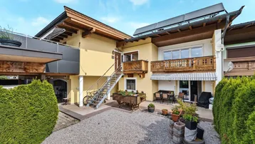 Traditionelles Haus mit gelber Fassade, Holzbalkonen und Solaranlage auf dem Dach.
