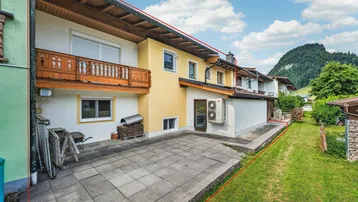 Große gepflasterte Terrasse hinter dem Haus mit Rasenfläche und Bergblick.