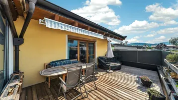 Große Holzterrasse mit Esstisch, Markise und weitem Blick auf die umliegende Berglandschaft.