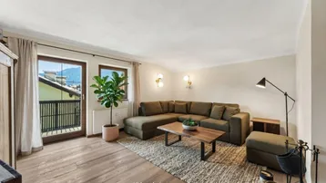 Helles Wohnzimmer mit modernem Ecksofa, Holzboden und Balkonzugang mit Bergblick.