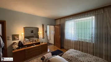 Helles Schlafzimmer mit klassischer Einrichtung und Blick ins Grüne durch das große Fenster.