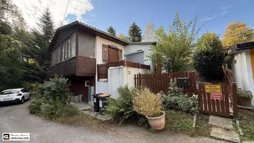Außenansicht eines charmanten Hauses mit Holzbalkon, umgeben von üppiger Vegetation und Bäumen.