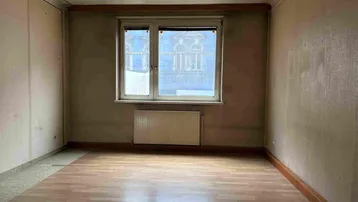 Leeres Zimmer mit Holzparkettboden und Fenster, das auf ein Gebäude blickt, bereit zur Renovierung.