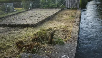 Grundstück am Fluss mit altem Holzschuppen und vorbereitetem Gartenbereich bei Sonnenuntergang.