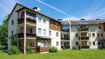 Mehrfamilienhaus mit Balkonen, Loggien und gepflegter Grünfläche unter blauem Himmel.