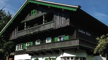 Traditionelles Landhaus "Stefanie" mit Holzbalkonen und grünen Fensterläden unter blauem Himmel.
