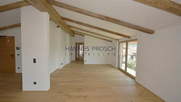 Geräumiger, heller Wohnbereich mit Holzbalken, hohen Decken und Zugang zu einem Außenbereich.