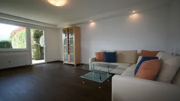 Helles Wohnzimmer mit dunklem Laminatboden, Sofa und Zugang zum Garten.