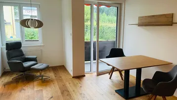 Helles Wohnzimmer mit Holzboden, gemütlichem Sessel und Zugang zum Balkon mit Grünblick.